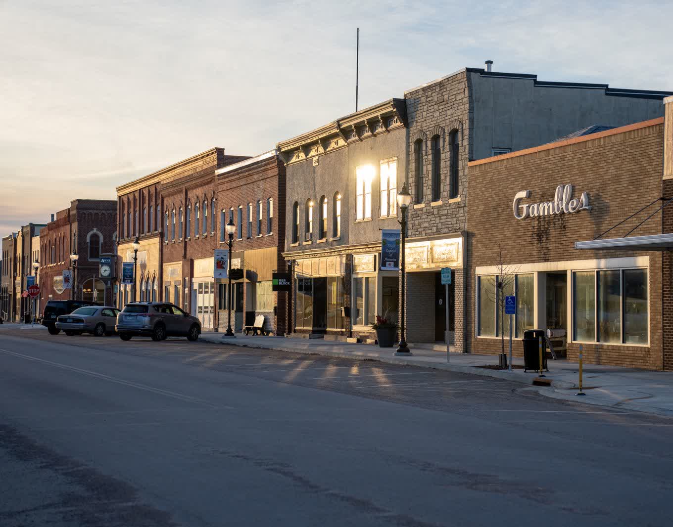 A small-city main street of brick storefronts in golden-hour light