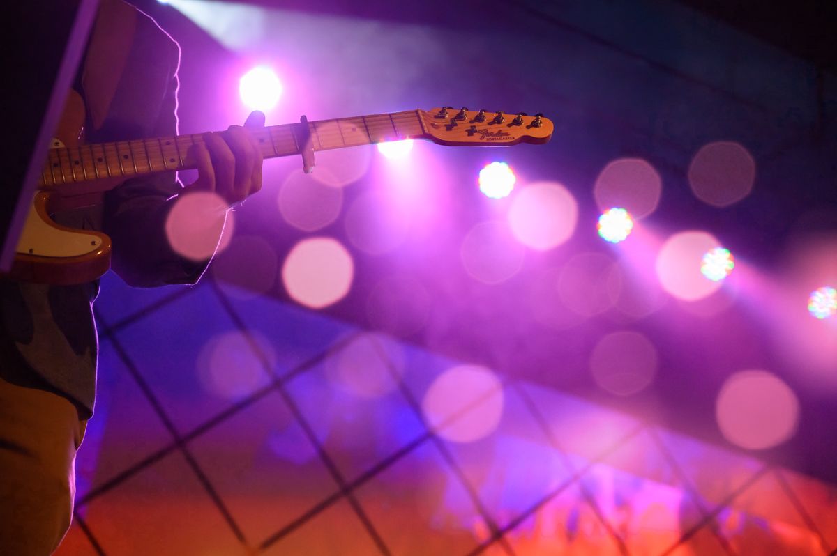 A guitarist under purple stage lights at a live concert